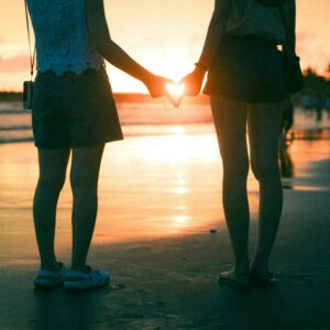 A couple stands on the beach at sunset, forming a heart shape with their hands. Perfect for romance themes.