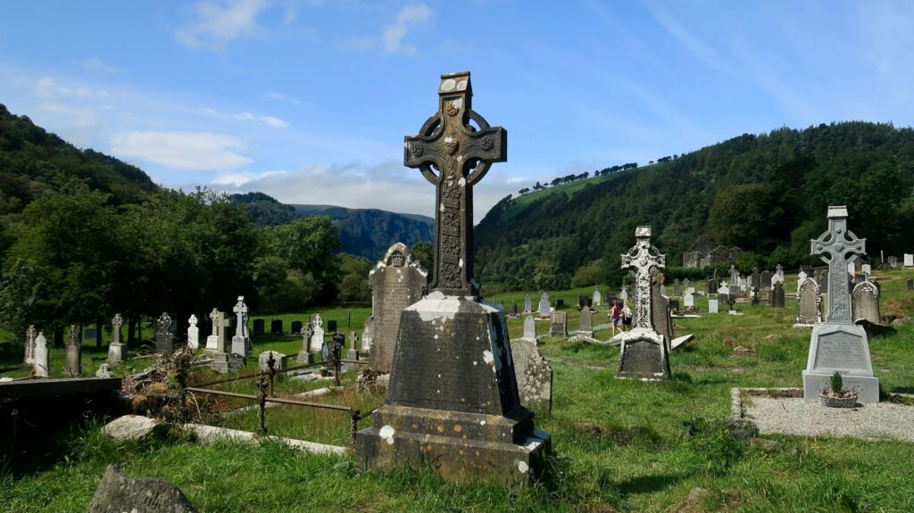 Ancient Celtic graveyard in Glendalough, Ireland with lush green hills and stone crosses.